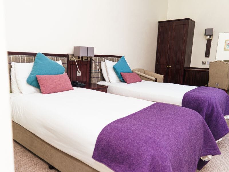 Twin beds with matching tweed blankets and cushions, check tweed headboards and neutral walls.