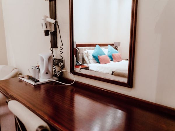 A neatly organised desk in a cosy bedroom with large mirror.