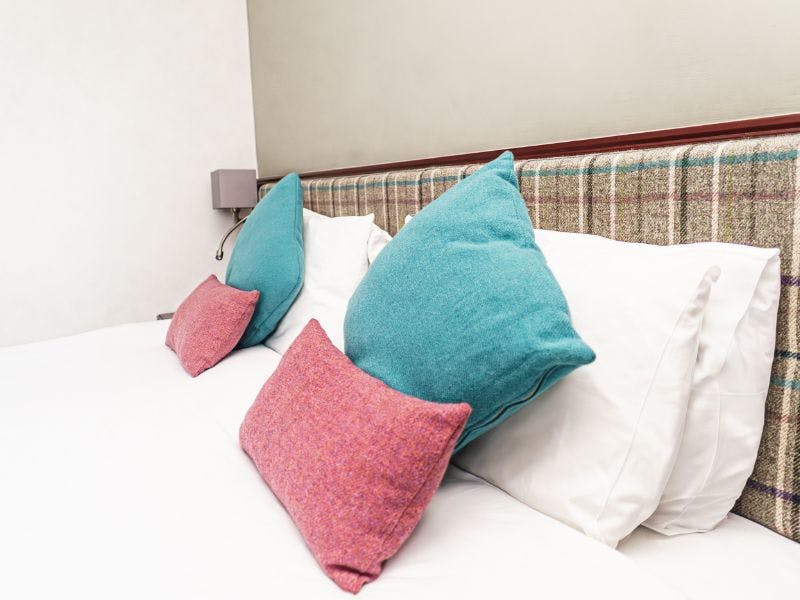 A cosy hotel bedroom with a comfortable bed with tweed cushions.