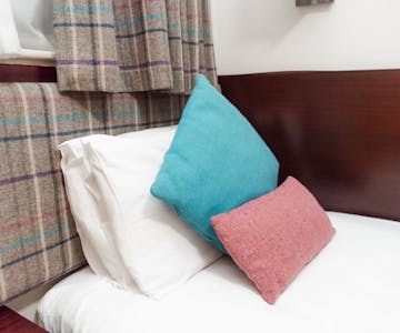 A cosy hotel single bedroom with a comfortable bed with colourful tweed cushions.