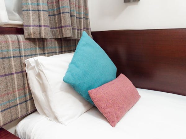 A cosy hotel single bedroom with a comfortable bed with colourful tweed cushions.