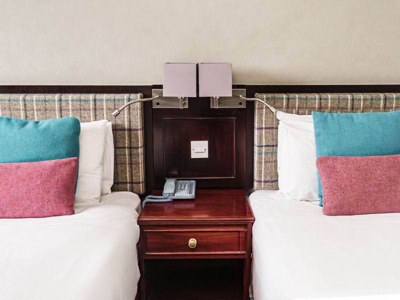 Two beds with blue and pink cushions and check tweed headboard.