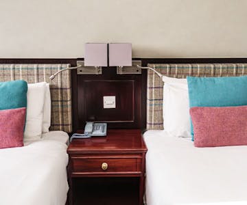 Two beds with blue and pink cushions and check tweed headboard.