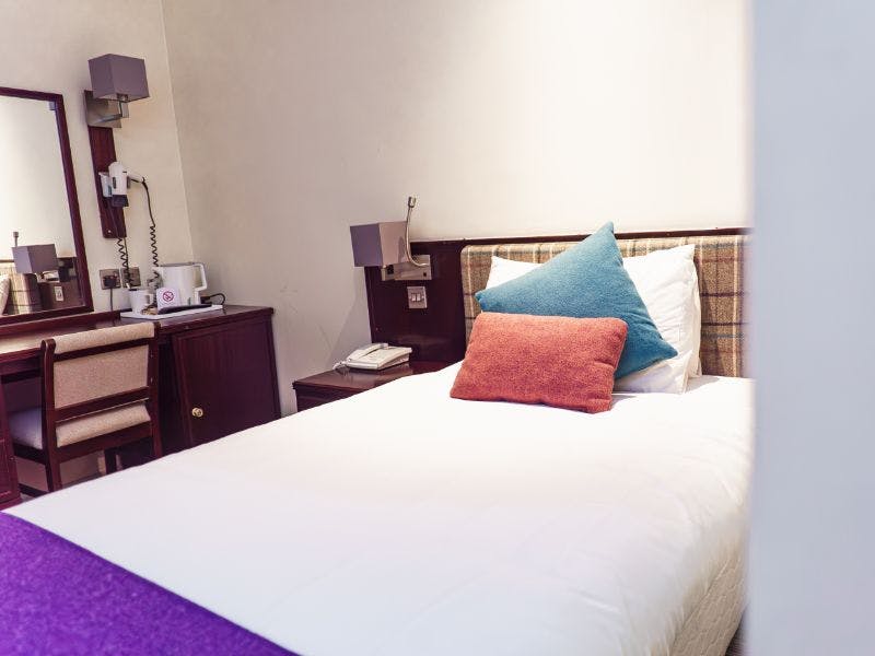 Single bed beds with colourful tweed blanket and cushions, check tweed headboard and neutral walls.