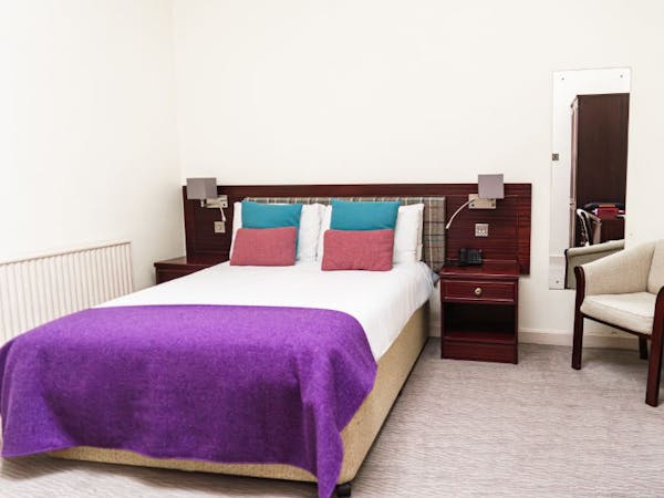 A cosy hotel bedroom with a comfortable bed with tweed cushions and throw.