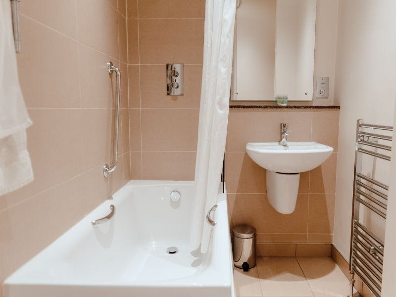 Modern bathroom with shower over bath and sink in neutral colours.