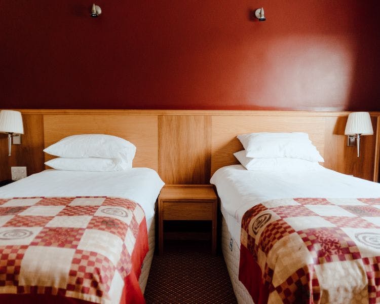 Twin room closeup with white bed linen, red check bed runner and deep red feature wall and wood panelling.