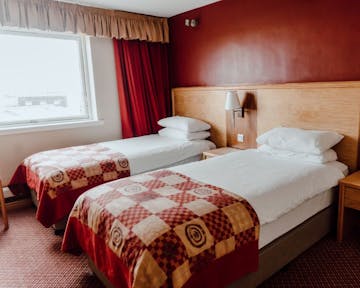 Twin room with white bed linen, red check bed runner, deep red walls with large window with complimentary coloured curtains.