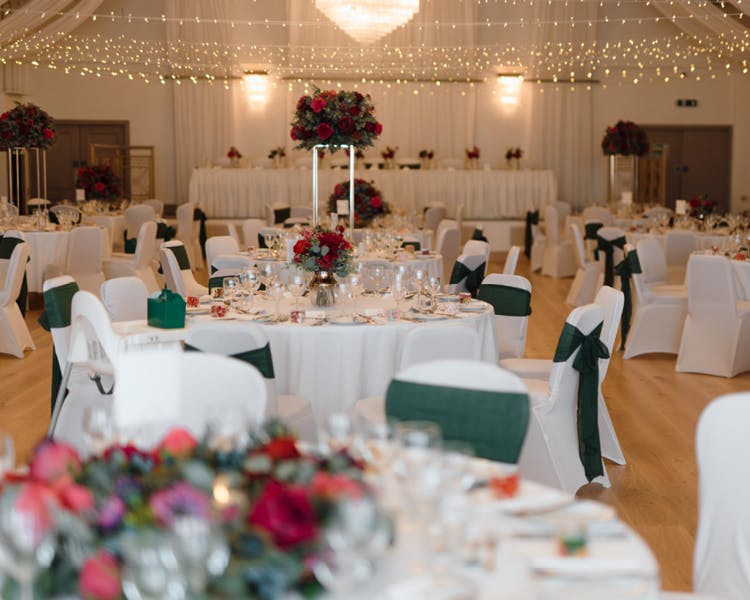 The Cabarfeidh ballroom set for a wedding reception, adorned with white and green tablecloths on each table.