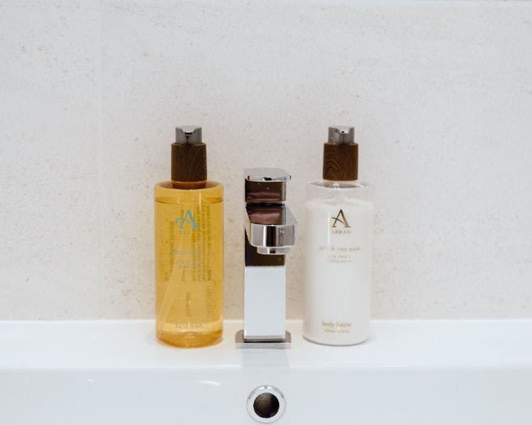 Bathroom closeup with fixed tap on brown sink suround and soap and hand cream dispensers.