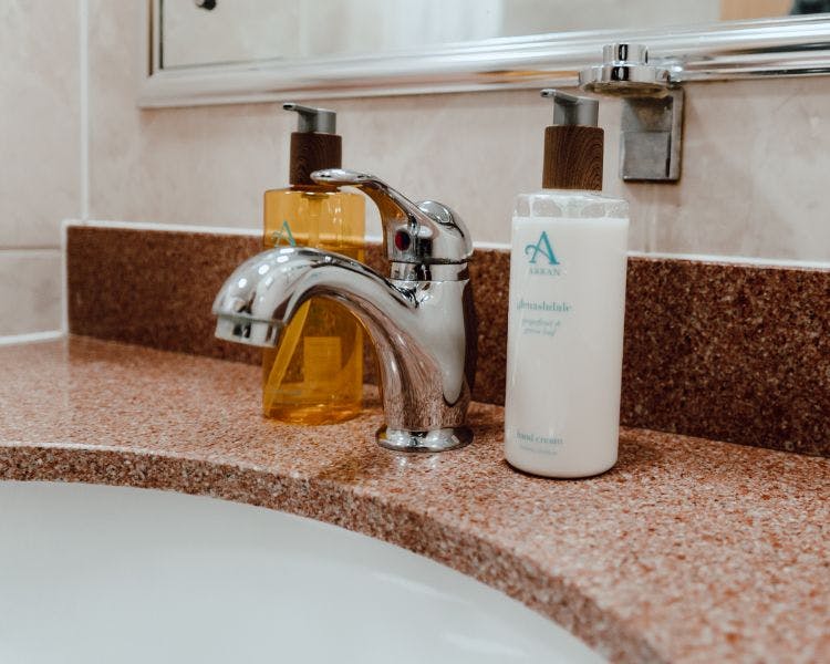 Bathroom closeup with fixed tap on brown sink suround and soap and hand cream dispensers.