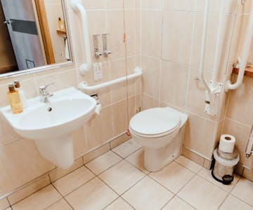 Accessible bathroom with neutral tiling, handrails. pull cord shower and white sink.