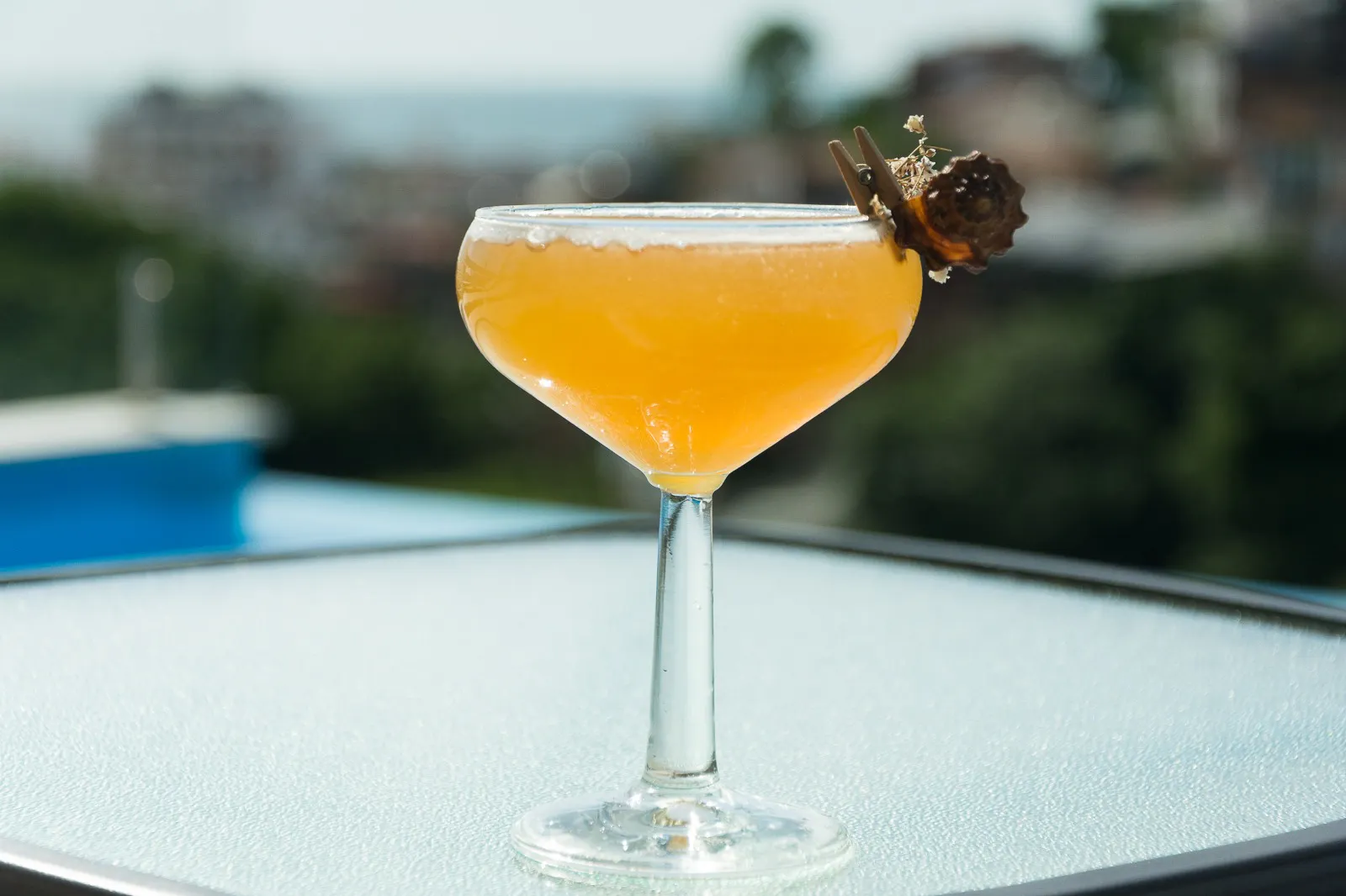 Golden cocktail served in a coupe glass beside the pool