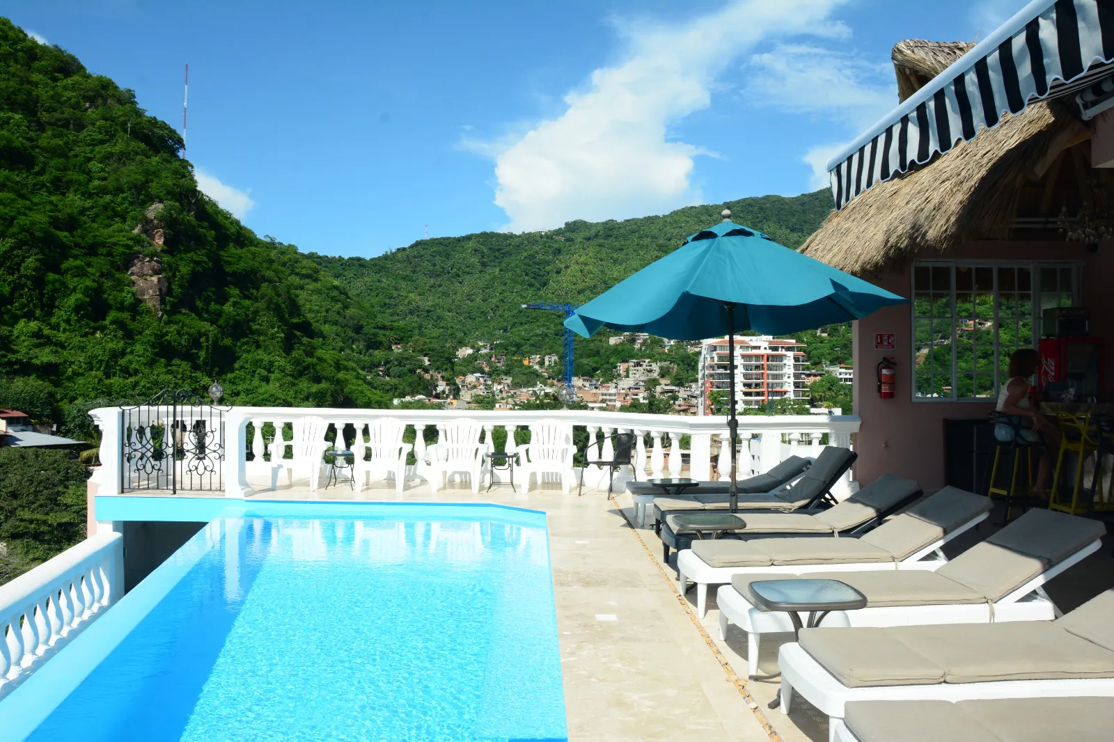 Outdoor pool with sun loungers, a blue umbrella and views of green hills
