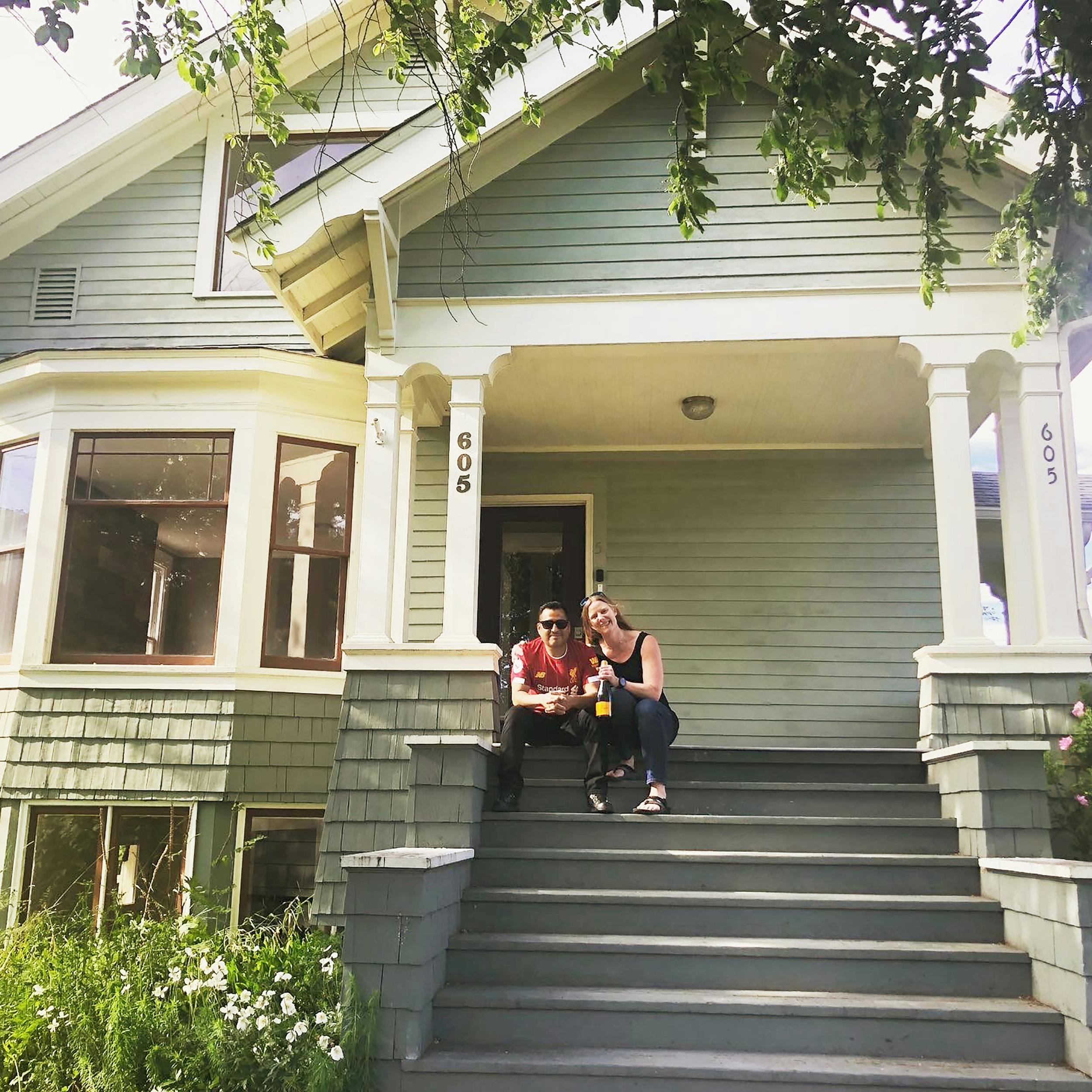 A couple sits on the front porch steps of a historic home.