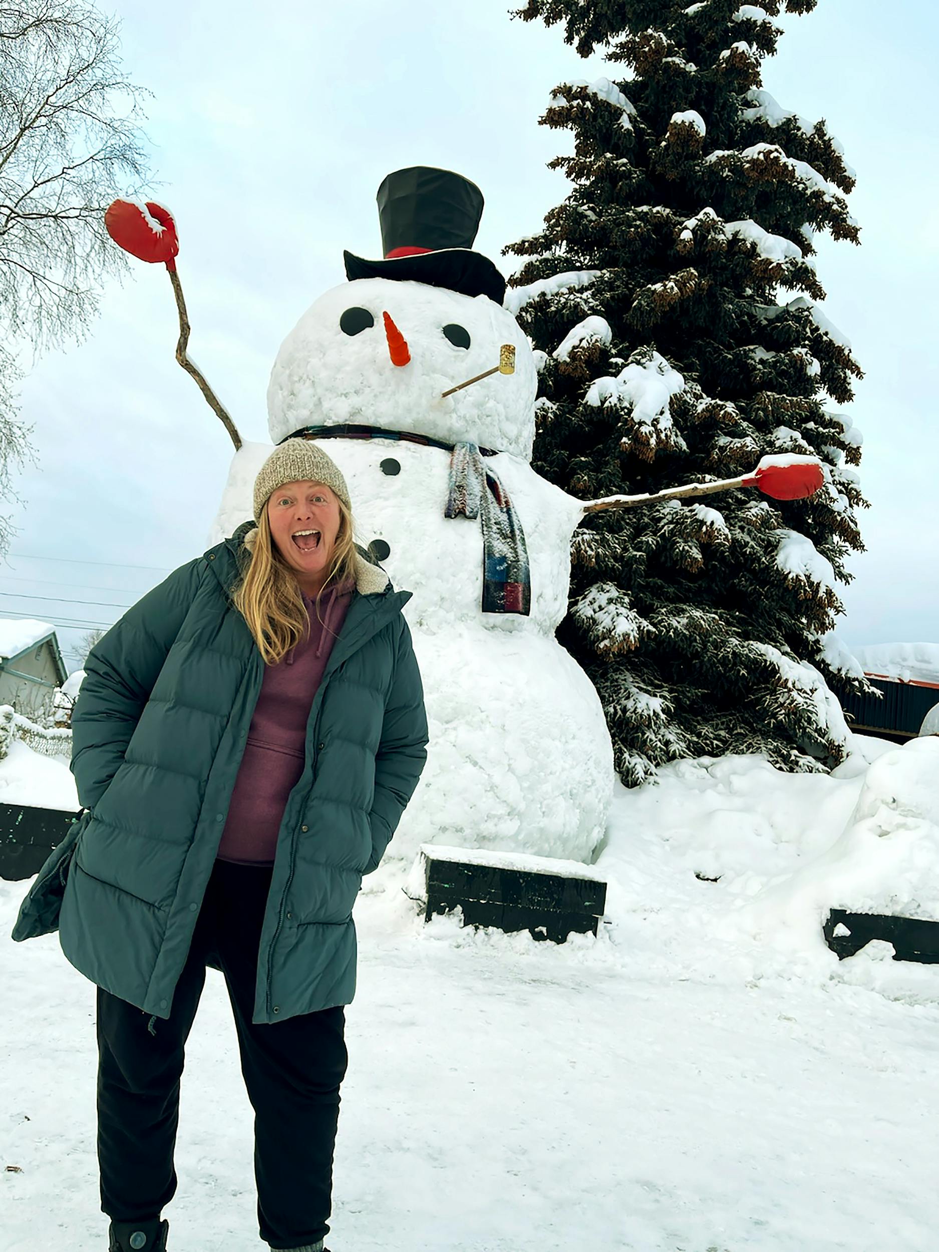 A woman in a winter coat stands in front of giant snow man in Anchorage.