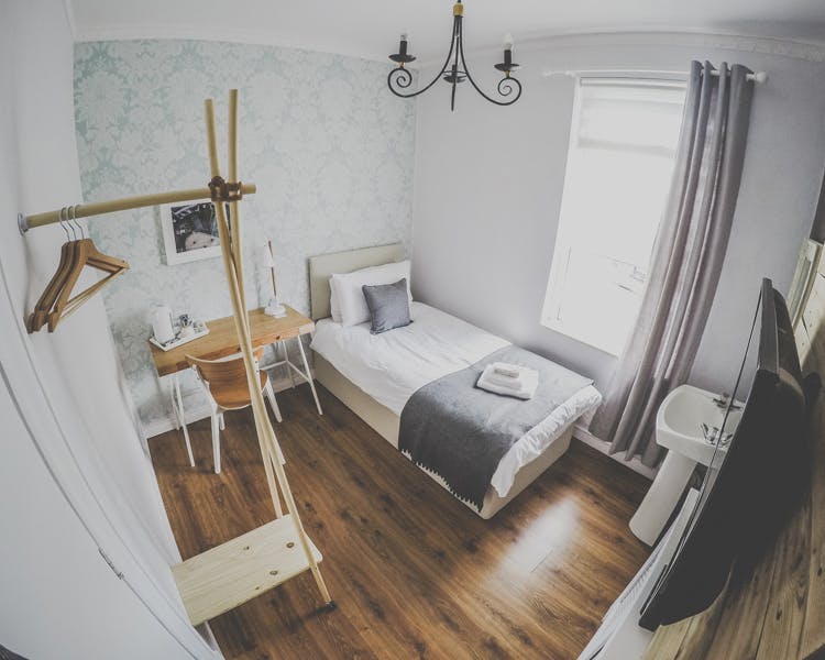 A beautifully decorated single room, coming along with a desk, hangers, TV and a sink