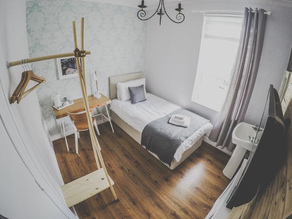 A beautifully decorated single room, coming along with a desk, hangers, TV and a sink