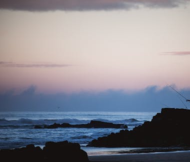 A fisherman stands on top of a rocky beach during the sunset.