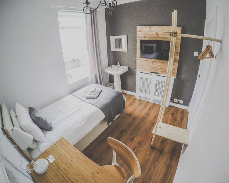 A beautifully decorated single room, coming along with a desk, hangers, TV and a sink