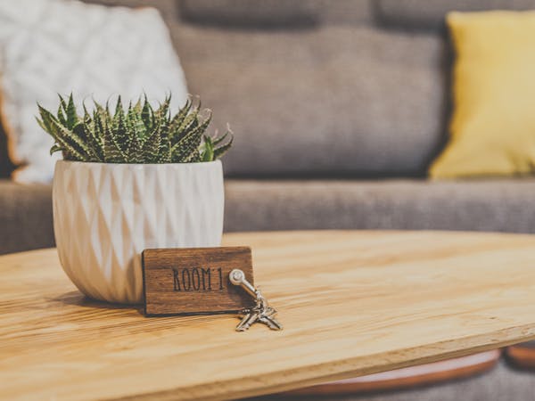 A cactus is on the table and the room key is in front of it. A couch with pillows standing in the background