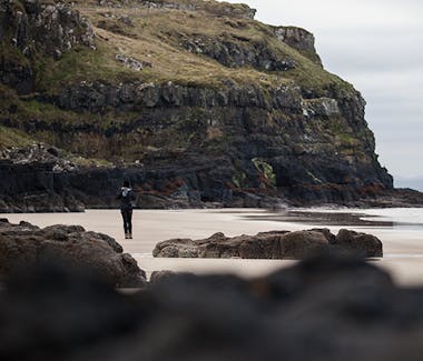 A person walking on a beach surrounded by rocks and cliffs