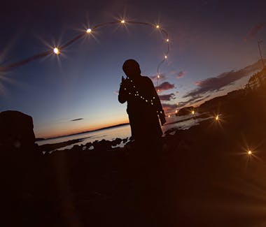 A person stands at the Portstewart Promenade during the sunset and holds fairy lights