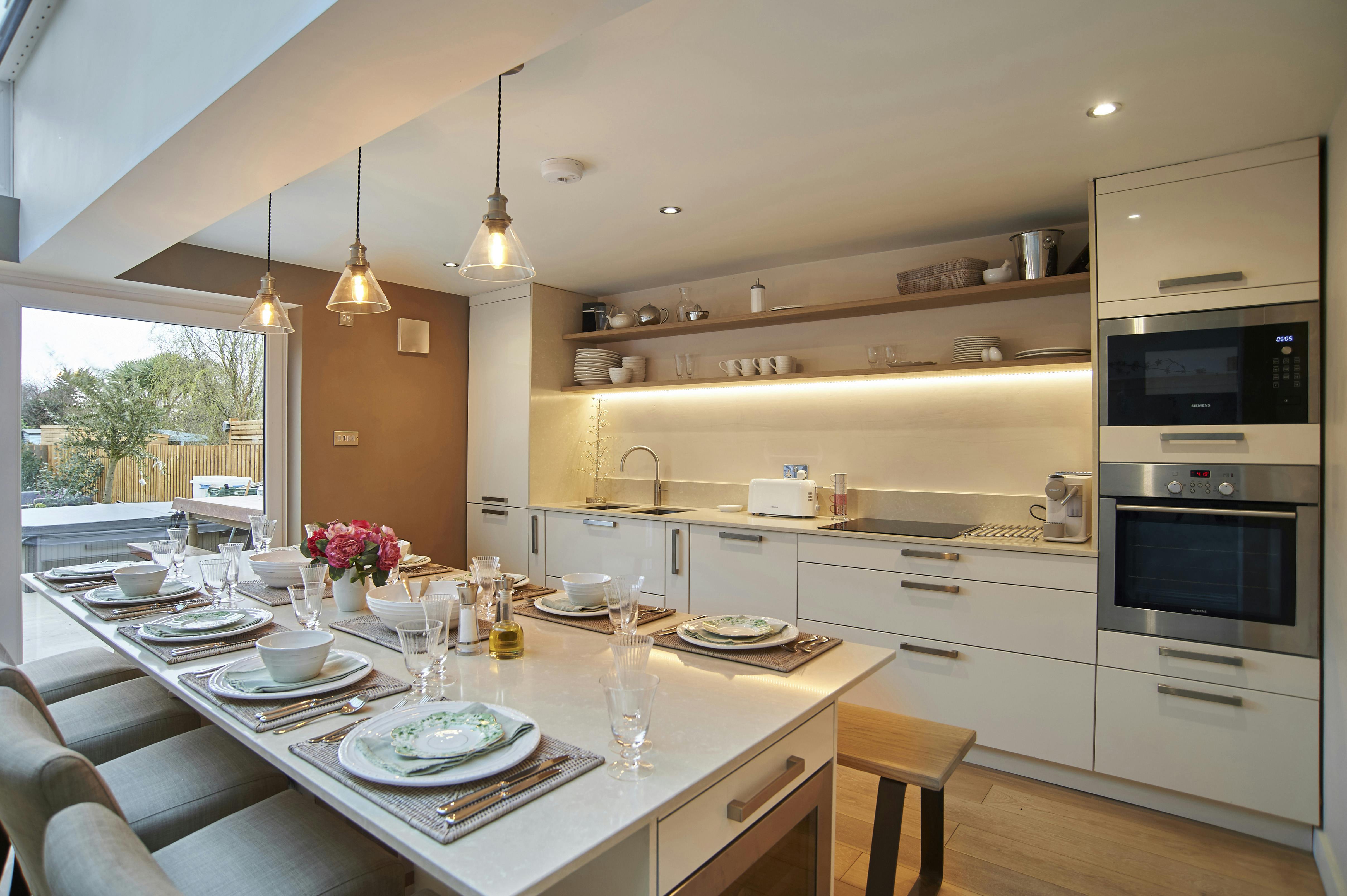 Kitchen view of table through to storage/surface preparation area of kitchen, storage shelves, fridge/freezer/oven/microwave