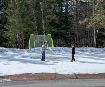 Image of Denise and the youngest Sinclair child hitting a baseball off of a tee into a net.