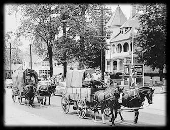 1950's black and white photo of The Victorian on Main with 2 horse drawn carriages and a parade passing in front of the house