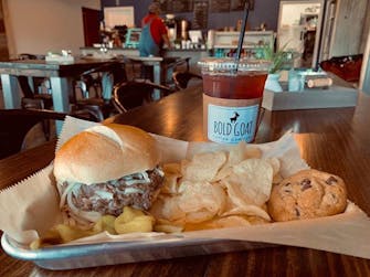 Sandwich, chips and a cookie on a plate. Bold Goat iced team in background