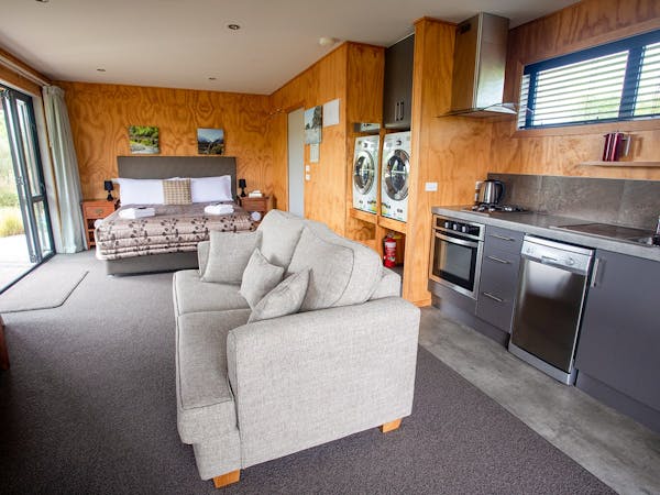 A modern-rustic living area with kitchen, couches, and large bed at Musterer's Accommodation, Fairlie.
