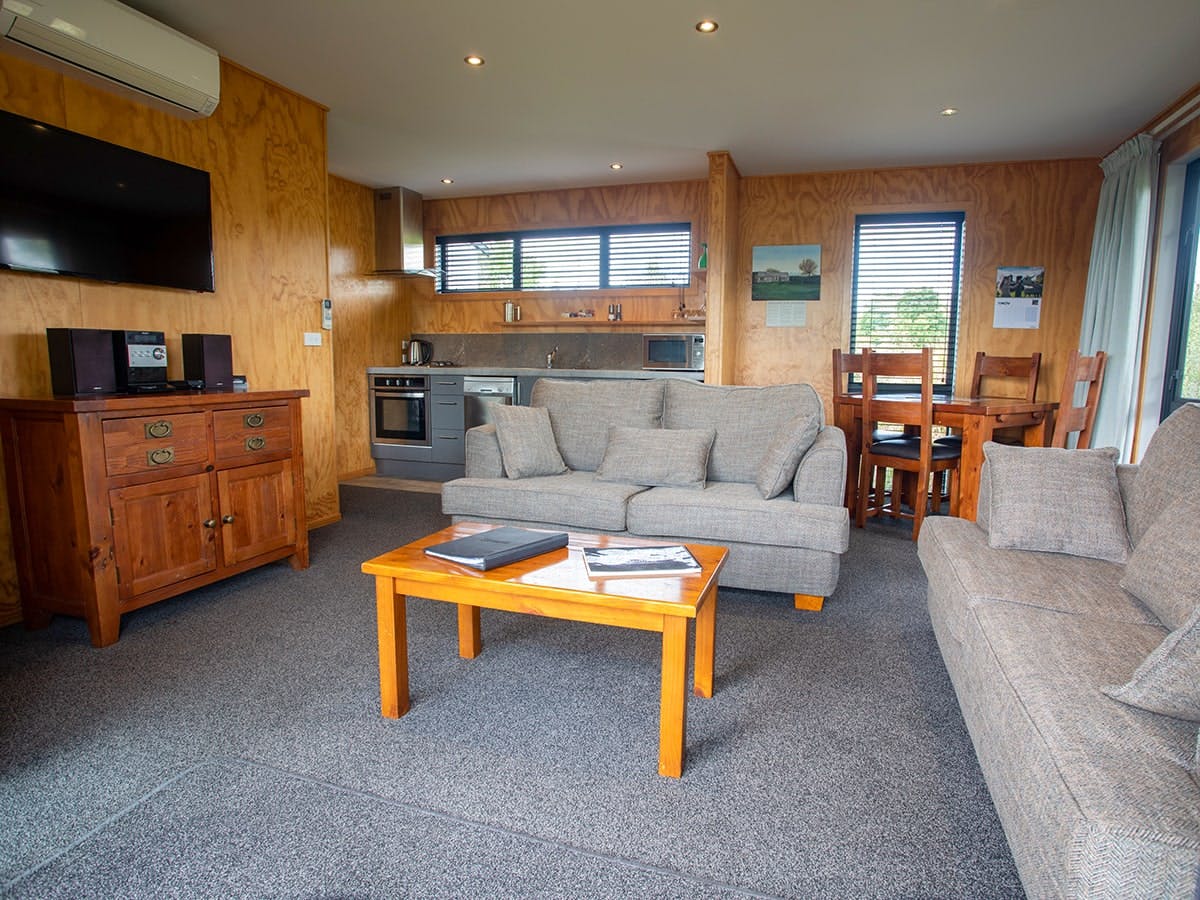 A modern-rustic living area with kitchen, couches, and wall tv at Musterer's Accommodation, Fairlie.