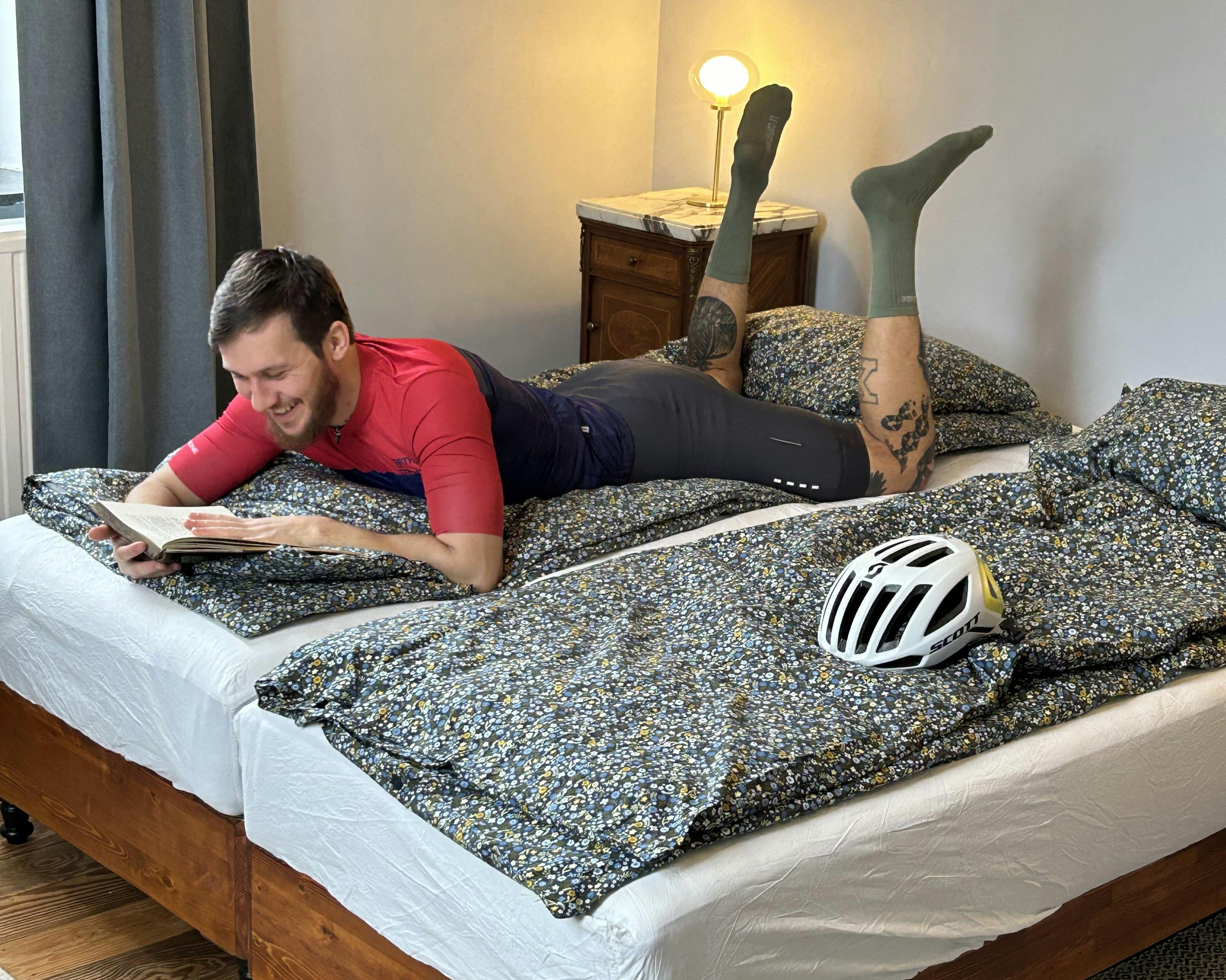 Cyclist relaxing on his bed with a book in one of the cozy rooms at La Maison Vienvenue after a ride.