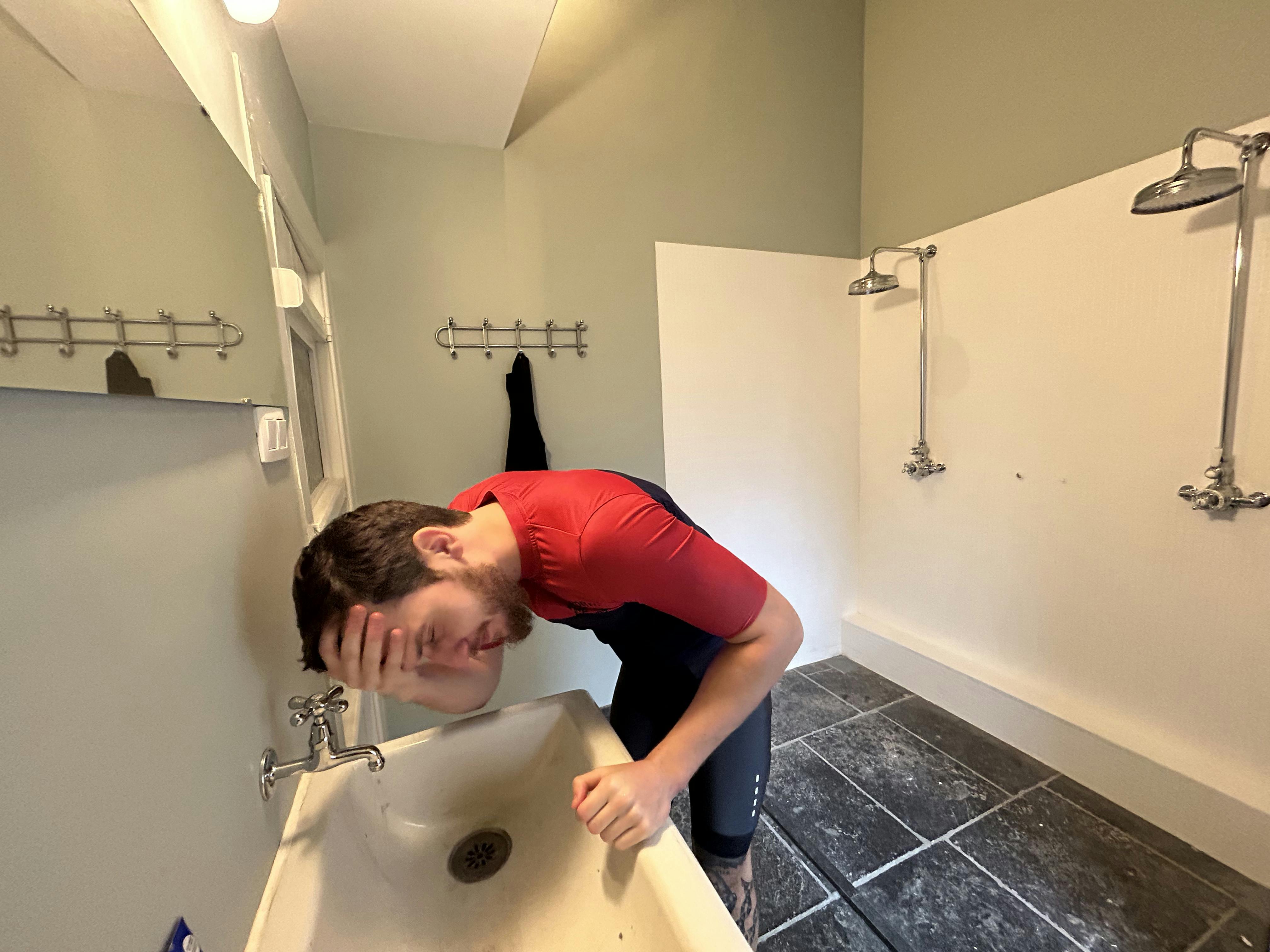 Cyclist washing their face at the sink in a shared, authentic bathroom with two showers at La Maison Vienvenue