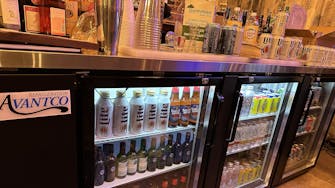 Bar stocked with various spirits, illuminated by a rhinestone 'Bar' sign.