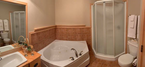 Salle de bain de la chambre Erable avec bain tourbillon et douche debout.