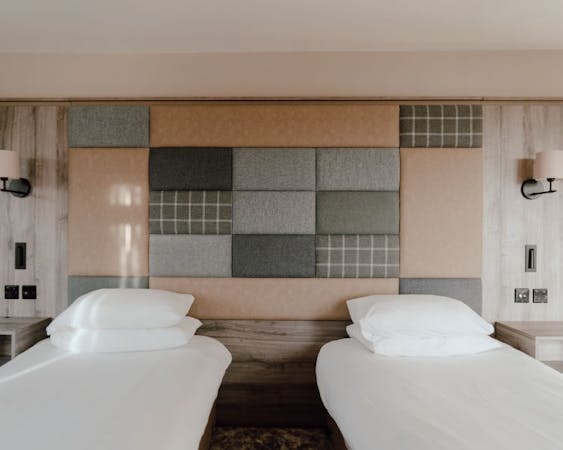 Twin beds in a hotel room with a tweed and leather fabric covered accent wall.