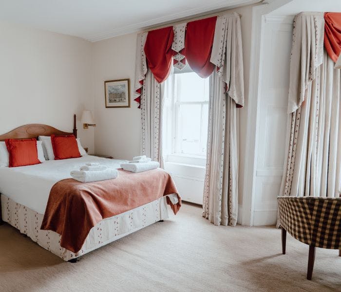 A cosy hotel room with a comfortable bed, a chair, and large windows offering a view over the marina to the Lews Castle.