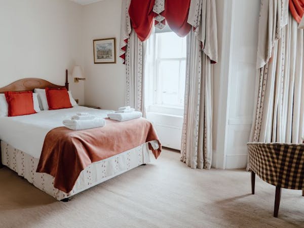A cosy hotel room with a comfortable bed, a chair, and large windows offering a view over the marina to the Lews Castle.