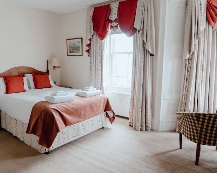A cosy hotel room with a comfortable bed, a chair, and large windows offering a view over the marina to the Lews Castle.