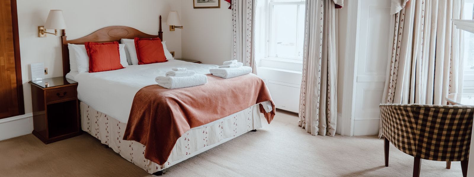 A cosy bed with crisp white sheets and a warm red throw with large windown with view to castle.