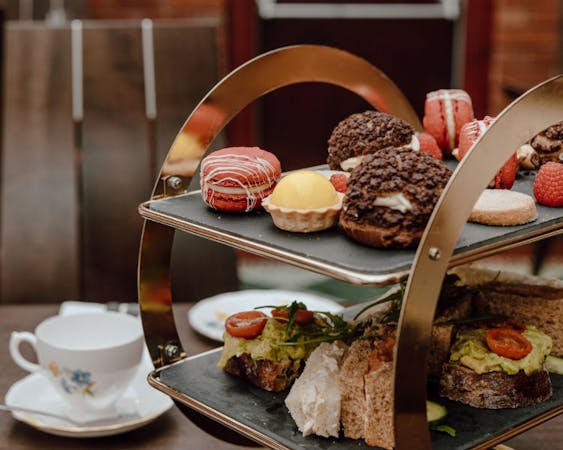 A table displaying an afternoon tea tray of pastries, including scone, macaron, lemon tart and sandwich.