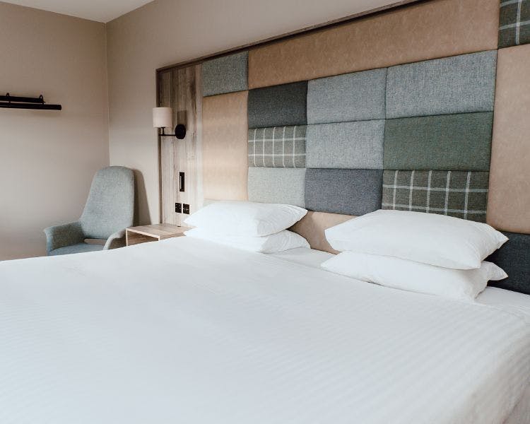 Double bed in a hotel room with a tweed and leather fabric covered accent wall.