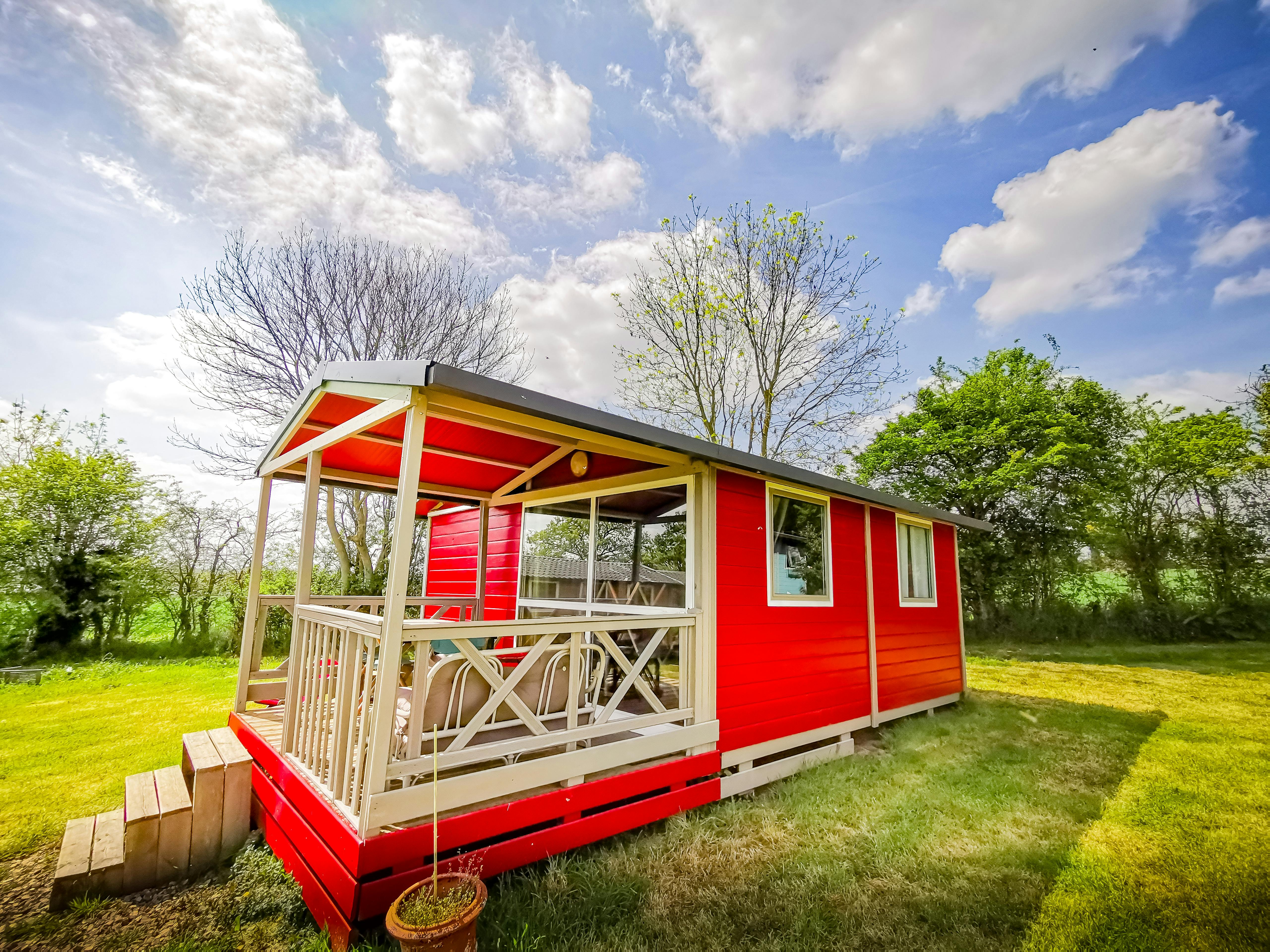 Vue extérieure du chalet rouge dans son intégralité avec sa terrasse et l'espace vert.