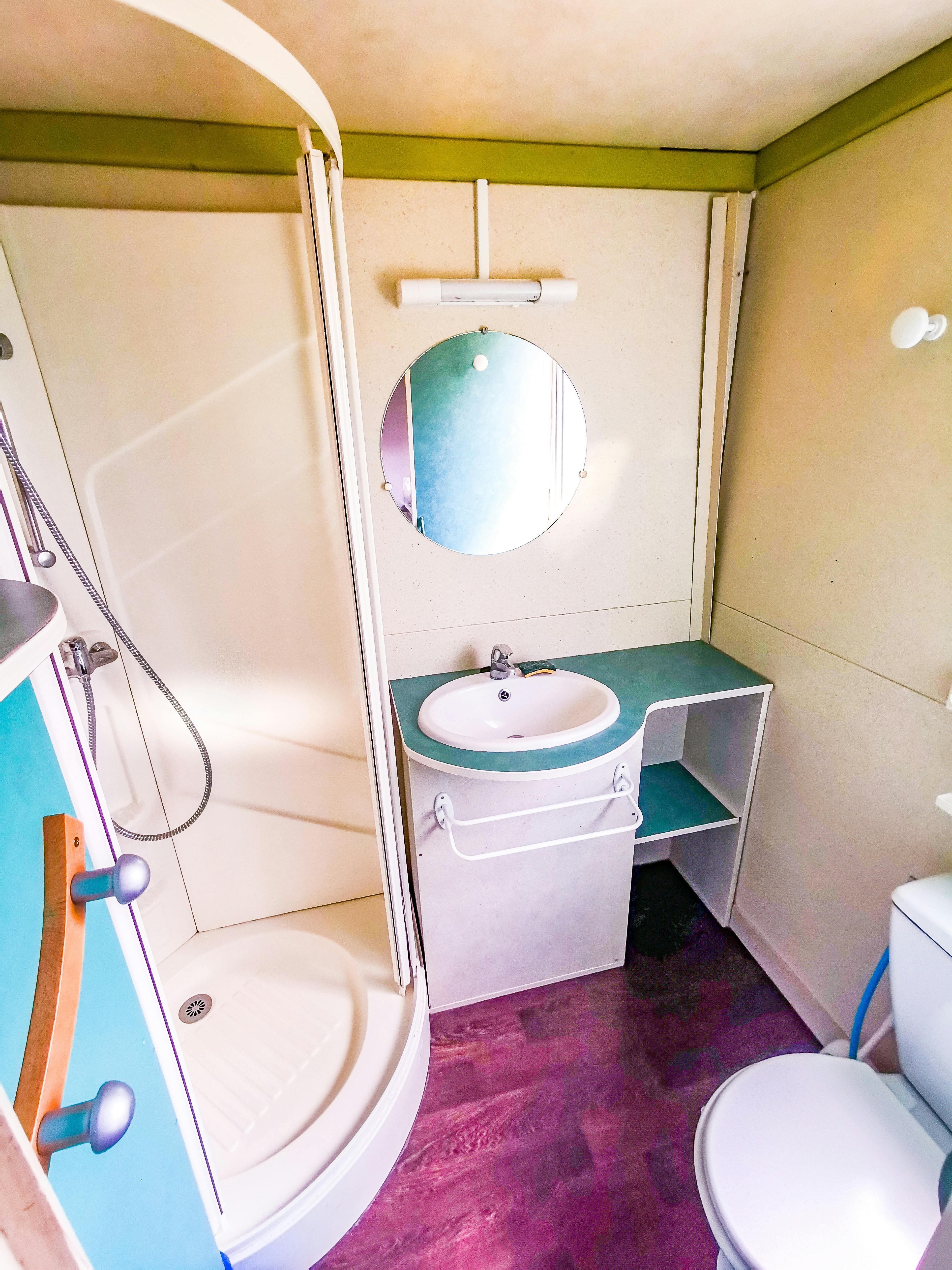Intérieur du chalet, salle de bain. Douche, toilettes, lavabos et miroir.