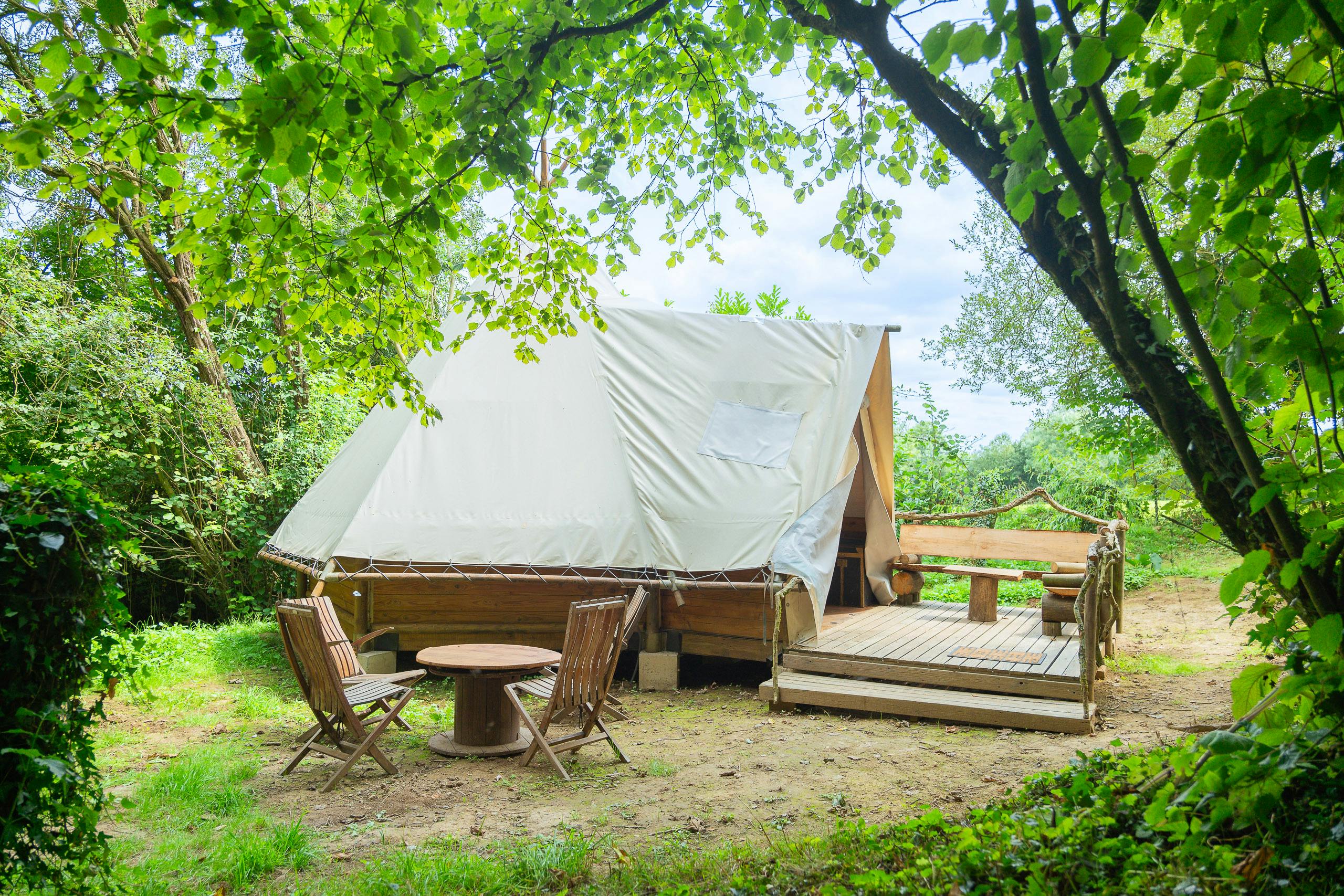 Au-Bonheur-Nomade - vue extérieure du tipi trappeur, à travers les arbres, mobilier d'été