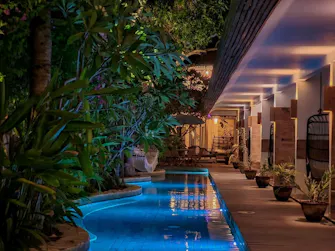 Tropical swimming pool surrounded by lush greenery and ambient evening lighting at Pesona Resort.