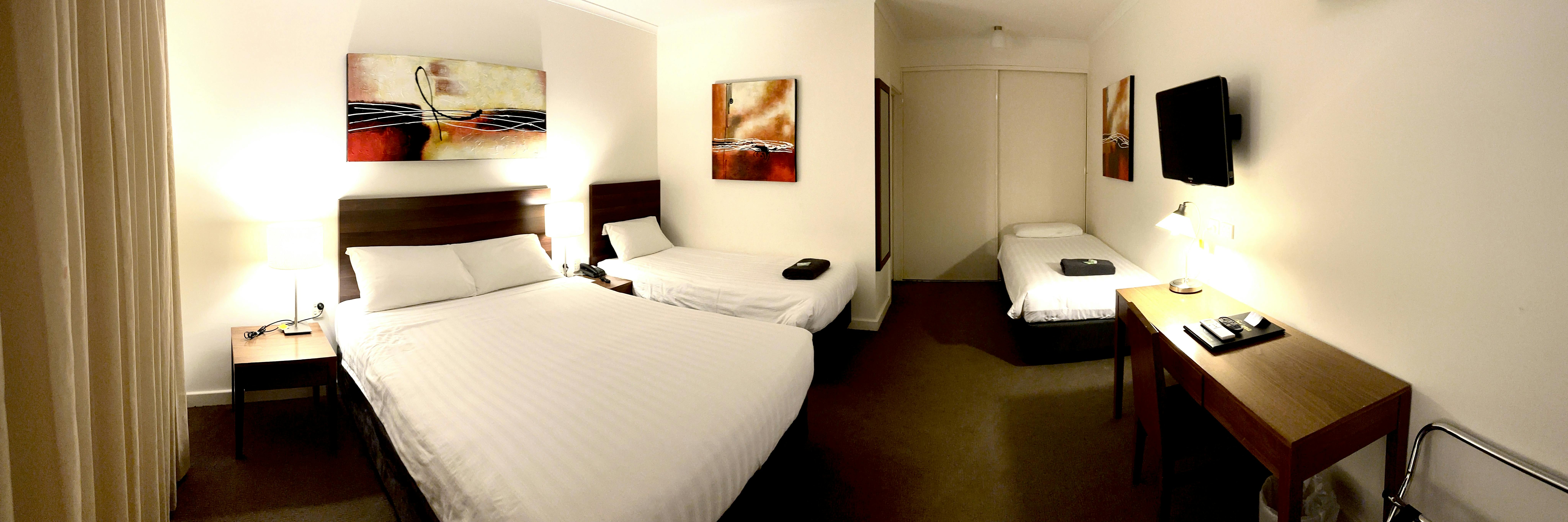 Modern room with 1 double, 2 single beds, artwork, TV, desk, and lamps.