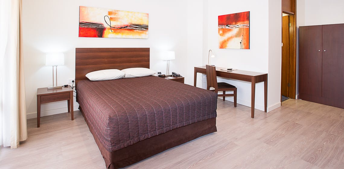 Modern room with queen bed, desk, artwork, and ample natural light.